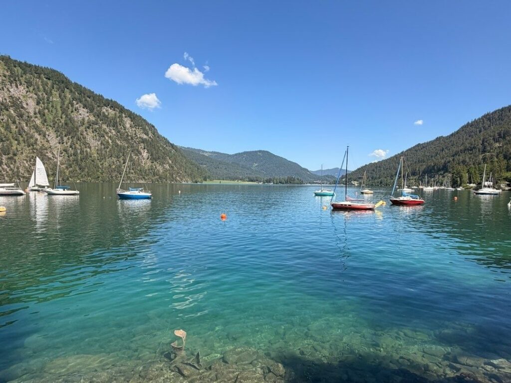 Segelboote auf einem klaren Bergsee zwischen bewaldeten Hängen