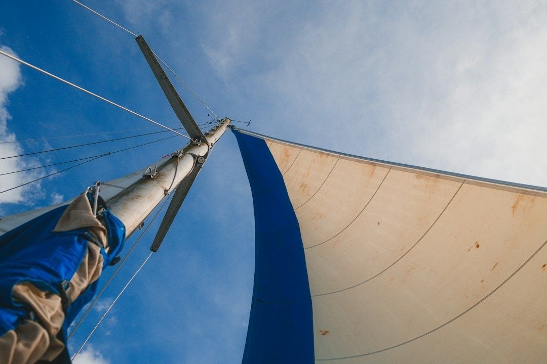 Blick nach oben auf einen Segelmast mit teilweise gesetztem blau-weißem Segel